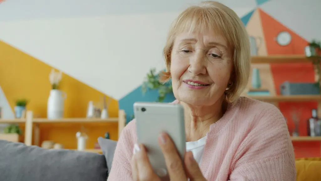 An older woman smiling as she uses her phone on the sofa at home